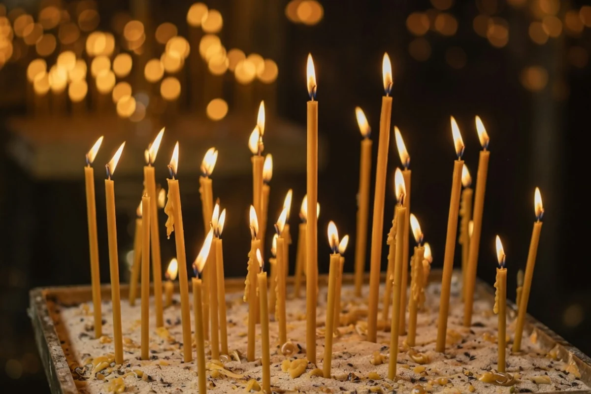 Thin beeswax candles burning in a church candle stand (illustrative image)
