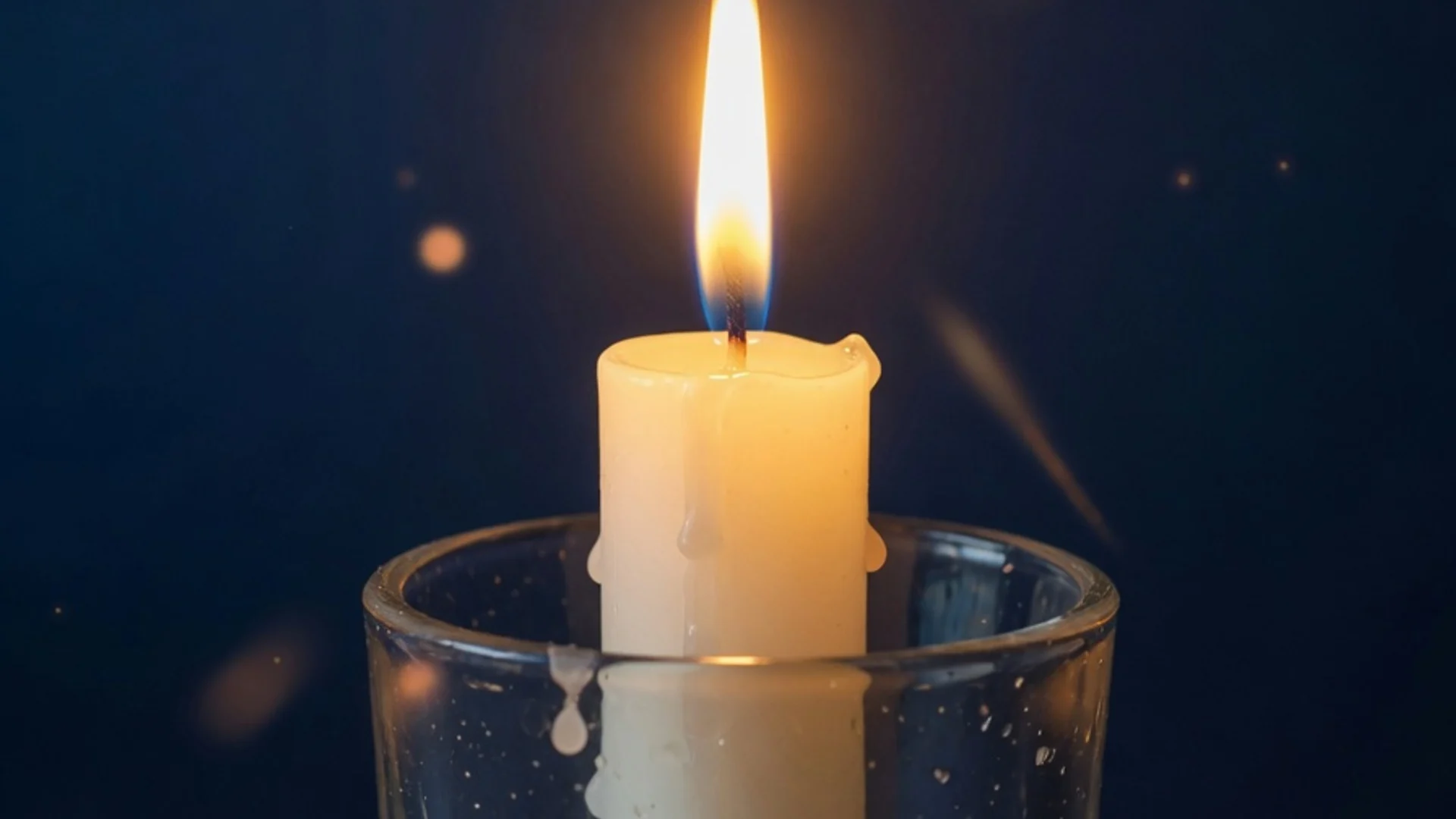 Single white candle burning against deep dark blue background