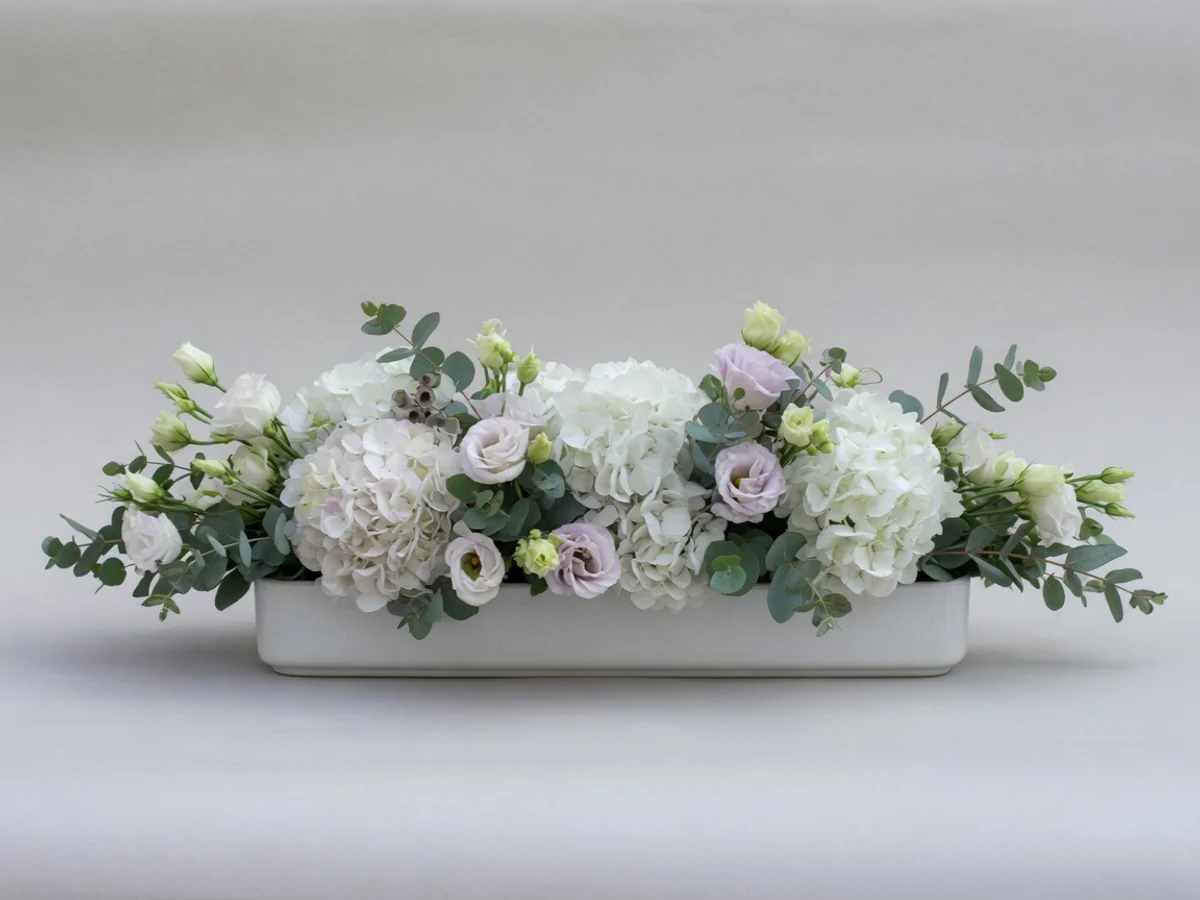 Low elongated condolences-table arrangement: white hydrangeas, eustoma and eucalyptus